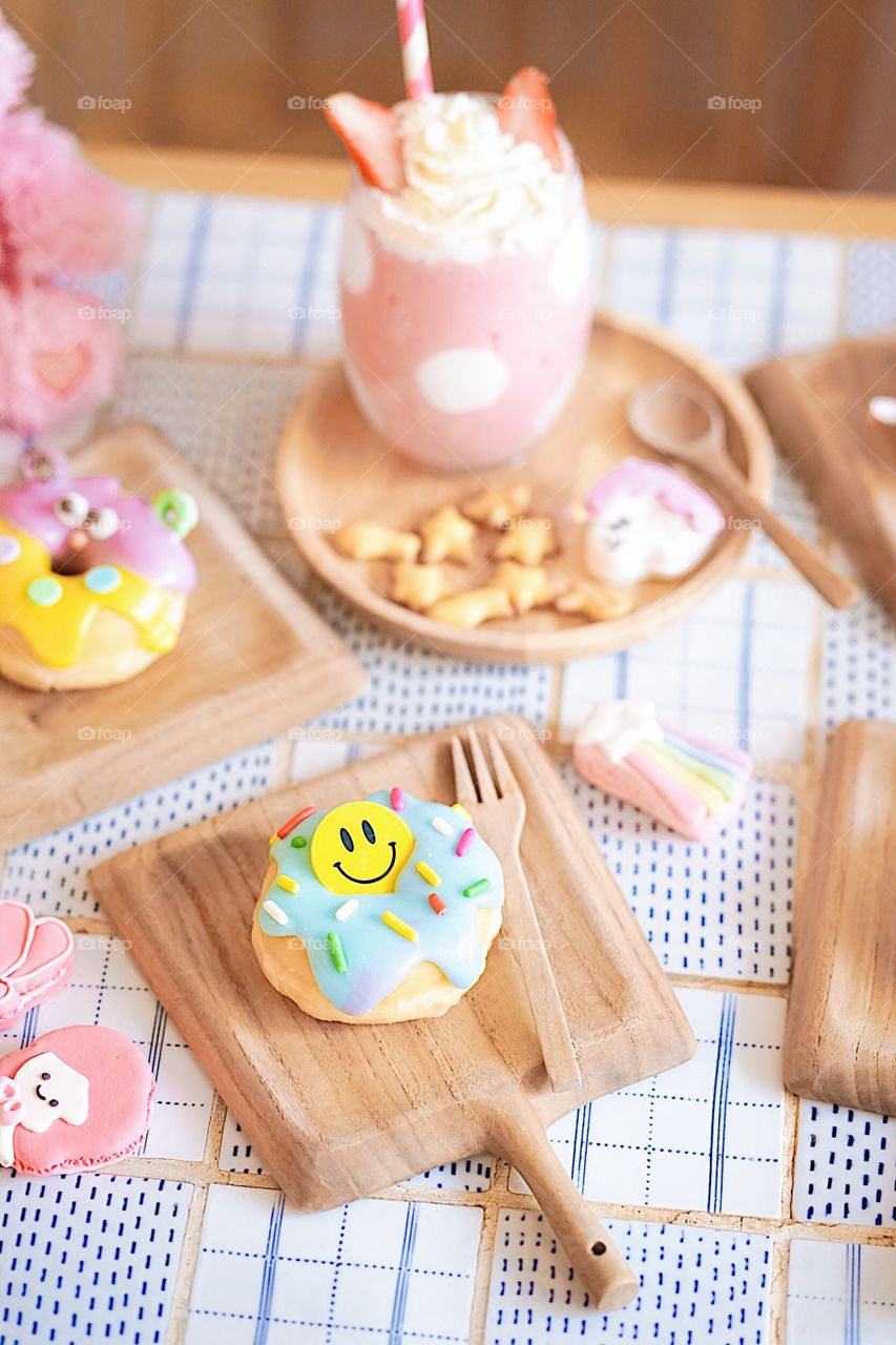 Cute donuts. Cute sugar glazed doughnut with happy smiling face and a cute monster doughnut served on a wooden table with a pink polka dot milkshake. Creative idea for fun birthday or private party.