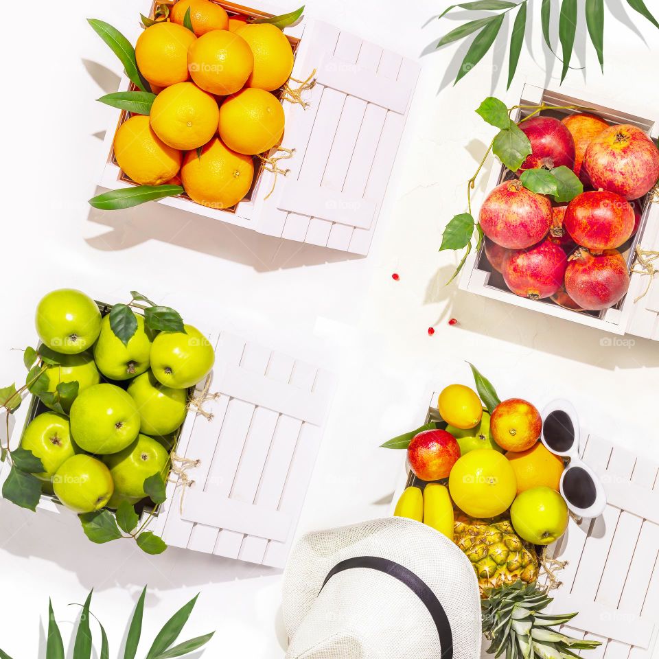 Summer tropical fruits. Oranges, apples, pomegranates and pineapple in white wooden boxes on a white background. Local market. Harvest Day. Summer sale of fruits