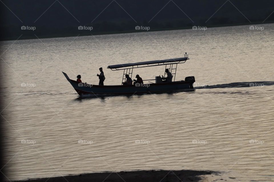 Silhouette of a boat with people on board at a lake at sunset
