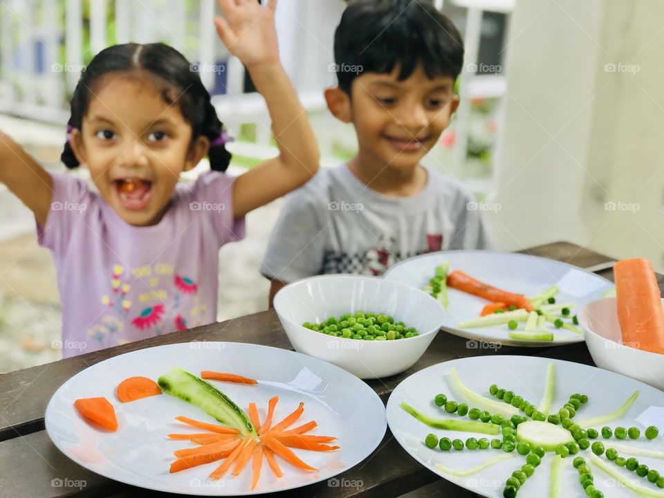 Kids enjoying by doing creative activities with vegetables. Here they made sun and coconut tree with Greenpeace and carrots.two kids are smiling and enjoying.