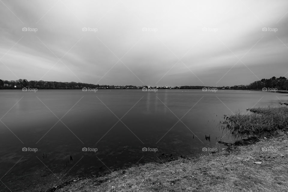 Ultra Wide Landscape Shot in Black and White of the land, shallow water, the lake, and downtown from a distance in the early night. This is a long exposure on a cloudy day. 