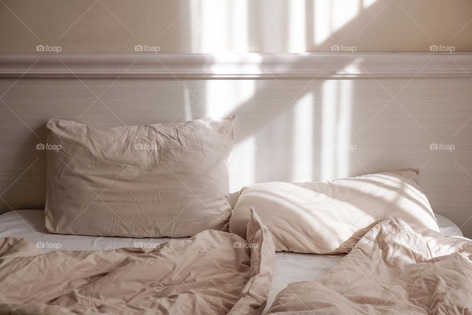 Bed with crumpled pillows and sheets in sunlight