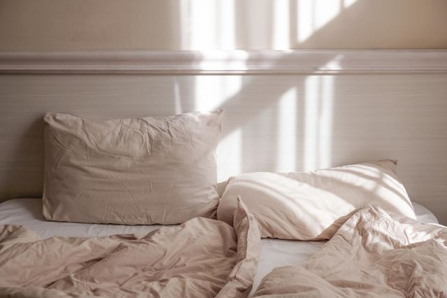 Bed with crumpled pillows and sheets in sunlight