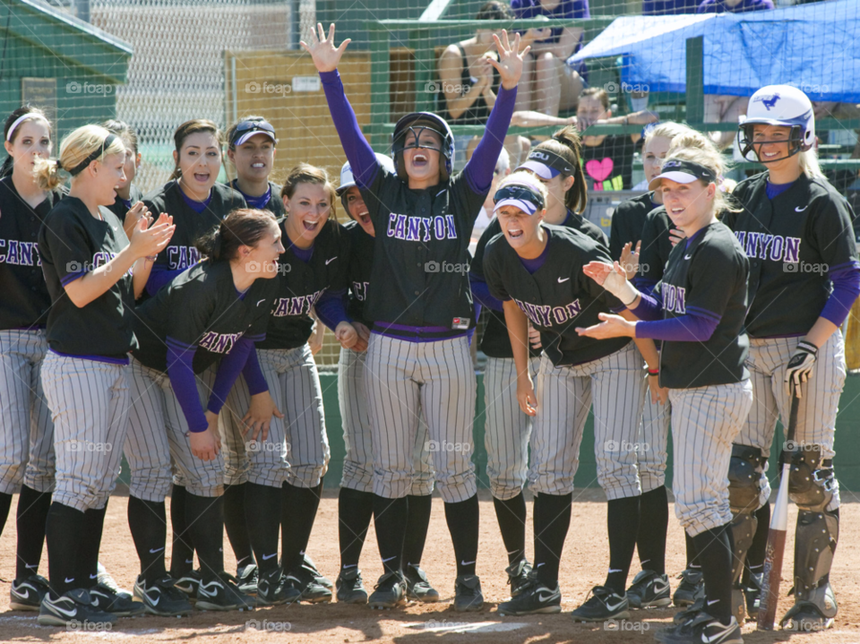softball players cheer a teammate after hitting a home run. women cheer teammate. women celebrate. by arizphotog