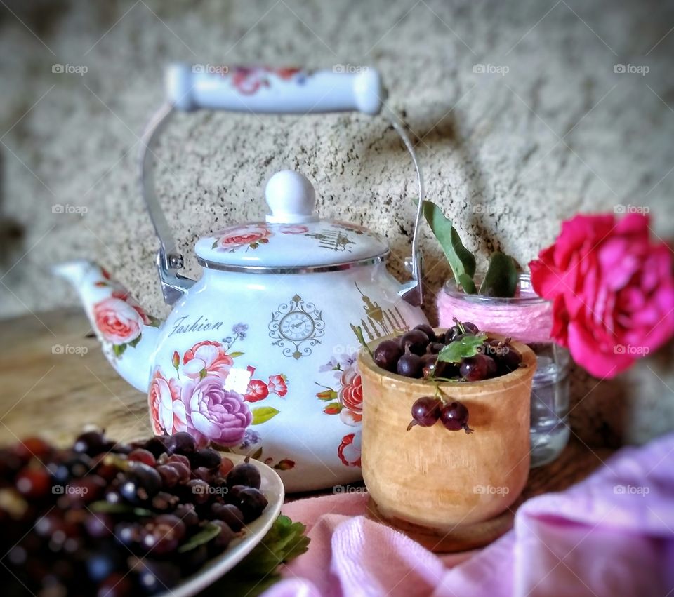 composition in pink shades: a teapot with pink flowers, a rose in a jar, pink napkins and currants