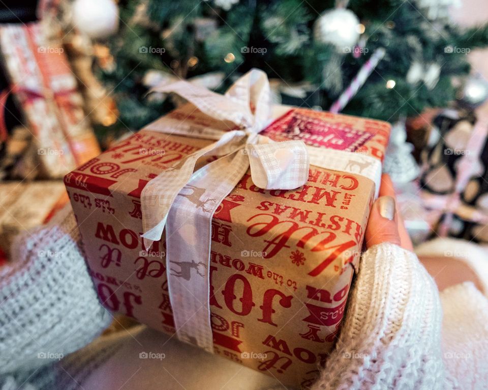 Close-up photo of woman holding wrapped christmas present in front of christmas tree