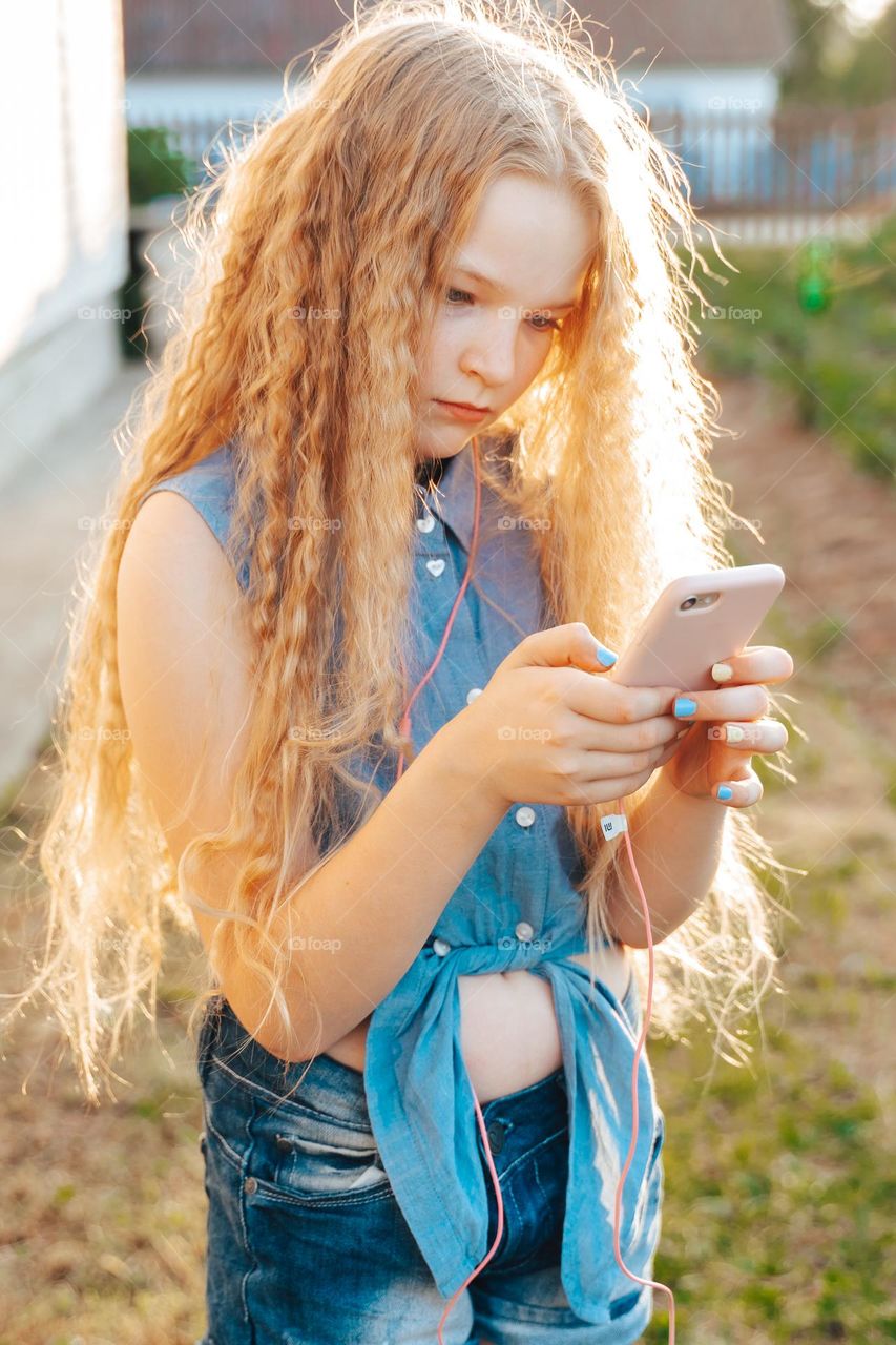 Beautiful curly long hair blond teen Gen z girl texting using phone 