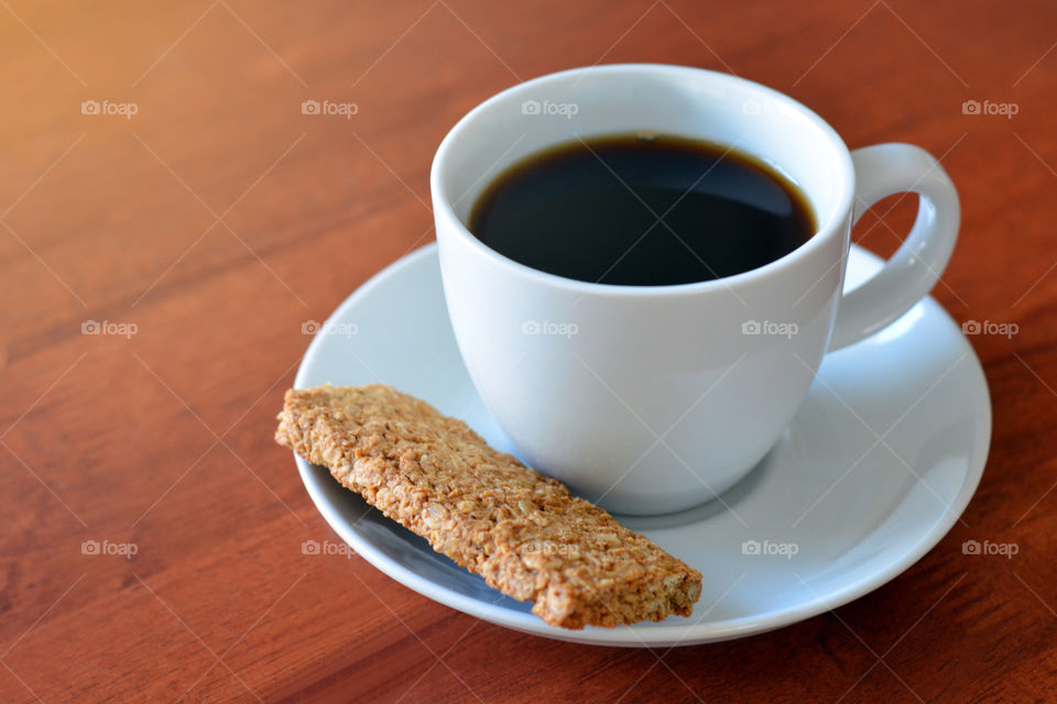 A cup of coffee with a piece of biscuit