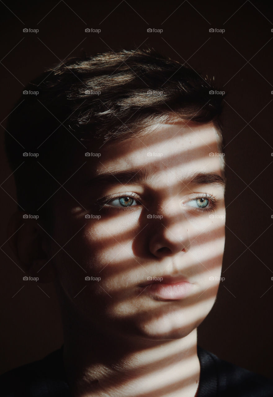 Portrait of boy looking away against wall with sunlight falling on his face. 