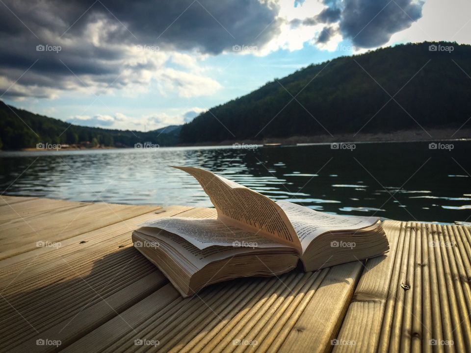 Open book on wooden ponton near the lake on a cloudy day