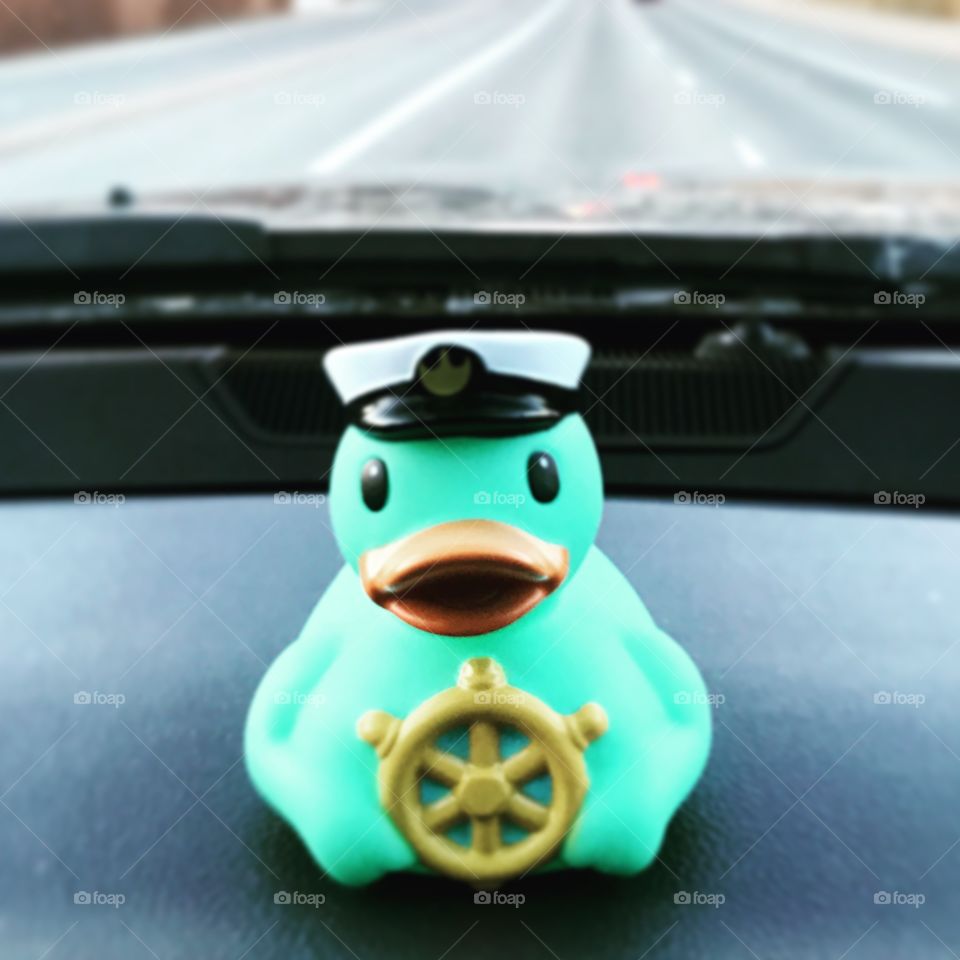 Bright blue rubber duck on dashboard wearing a captains hat 