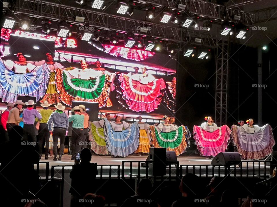 Group of men and women dressed in a colorful way, while dancing on a stage at night.