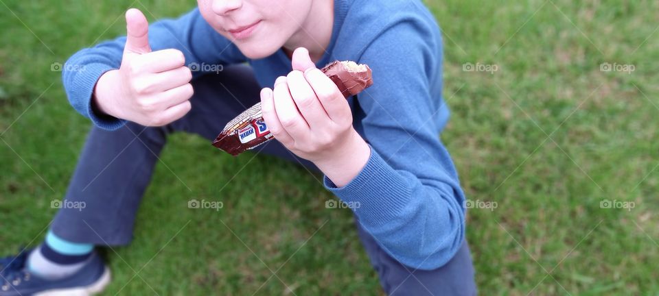 boy sitting on the grass and holding snickers