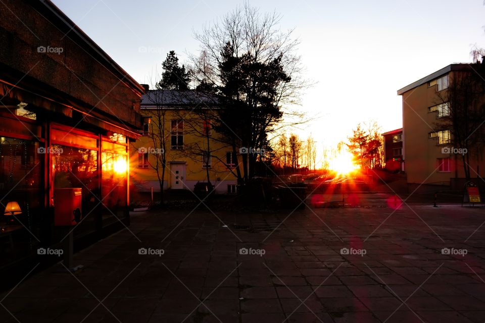 Two suns setting in an urban landscape. Sunset and reflection of a sunset from a big window create appearance of sun eyes in a suburban plaza in Helsinki, Finland in October evening.  
