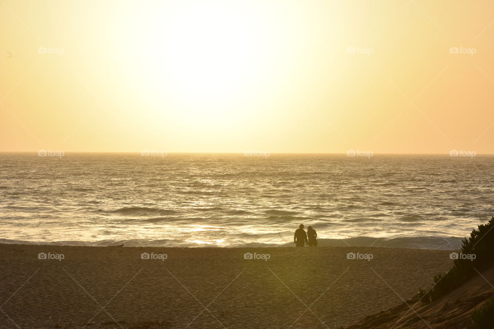 A couple enjoying sunset on a desolate beach.