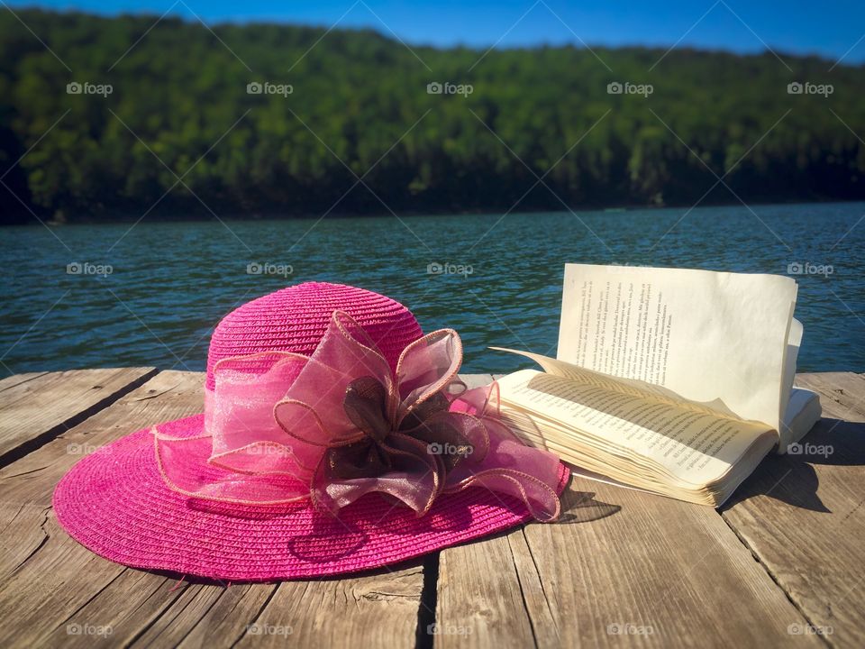 Reading near the lake: Summer hat and book on wooden deck near the lake