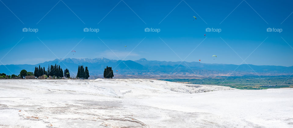 Paragliders in the sky above white like snow plateau of Pamukkale Travertines. Turkey. Famous for mineral rich thermal waters flowing down white terraces.