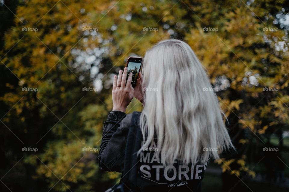blonde woman taking photo of fall foliage / autumn season