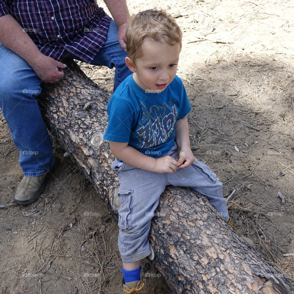 A boy and his great-uncle take a rest on a log while out hiking together in the forests of Central Oregon on a sunny summer day. 