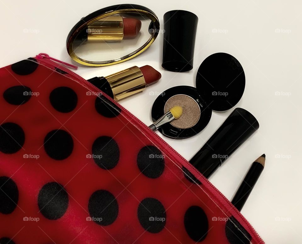 Black cased, unbranded make up items poke out from a red & black polka dot bag, with mirror