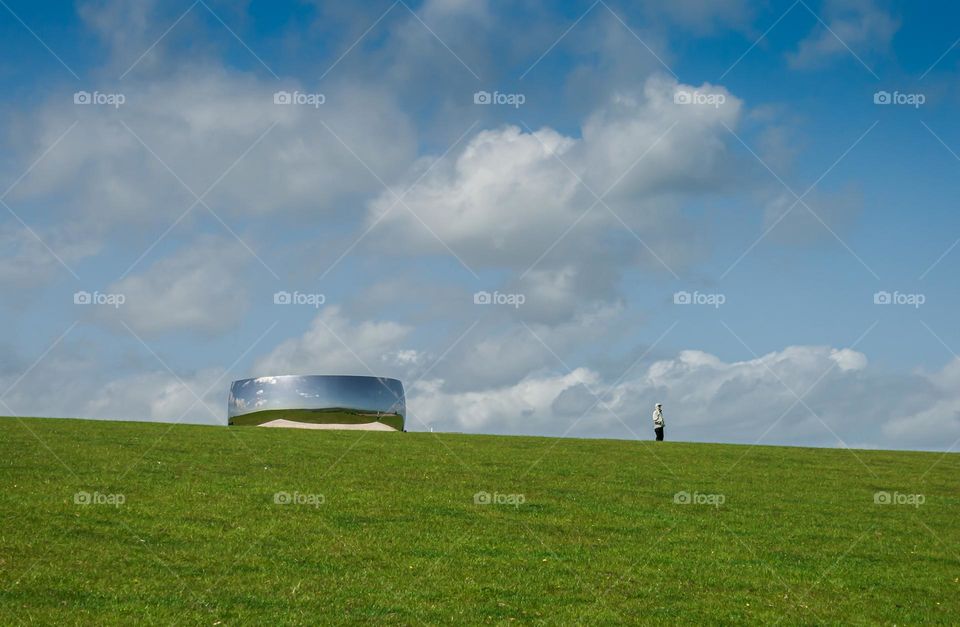 A man admires the view at the top of a hill, which is also exhibiting Anish Kapoor’s C-Curve (2007)