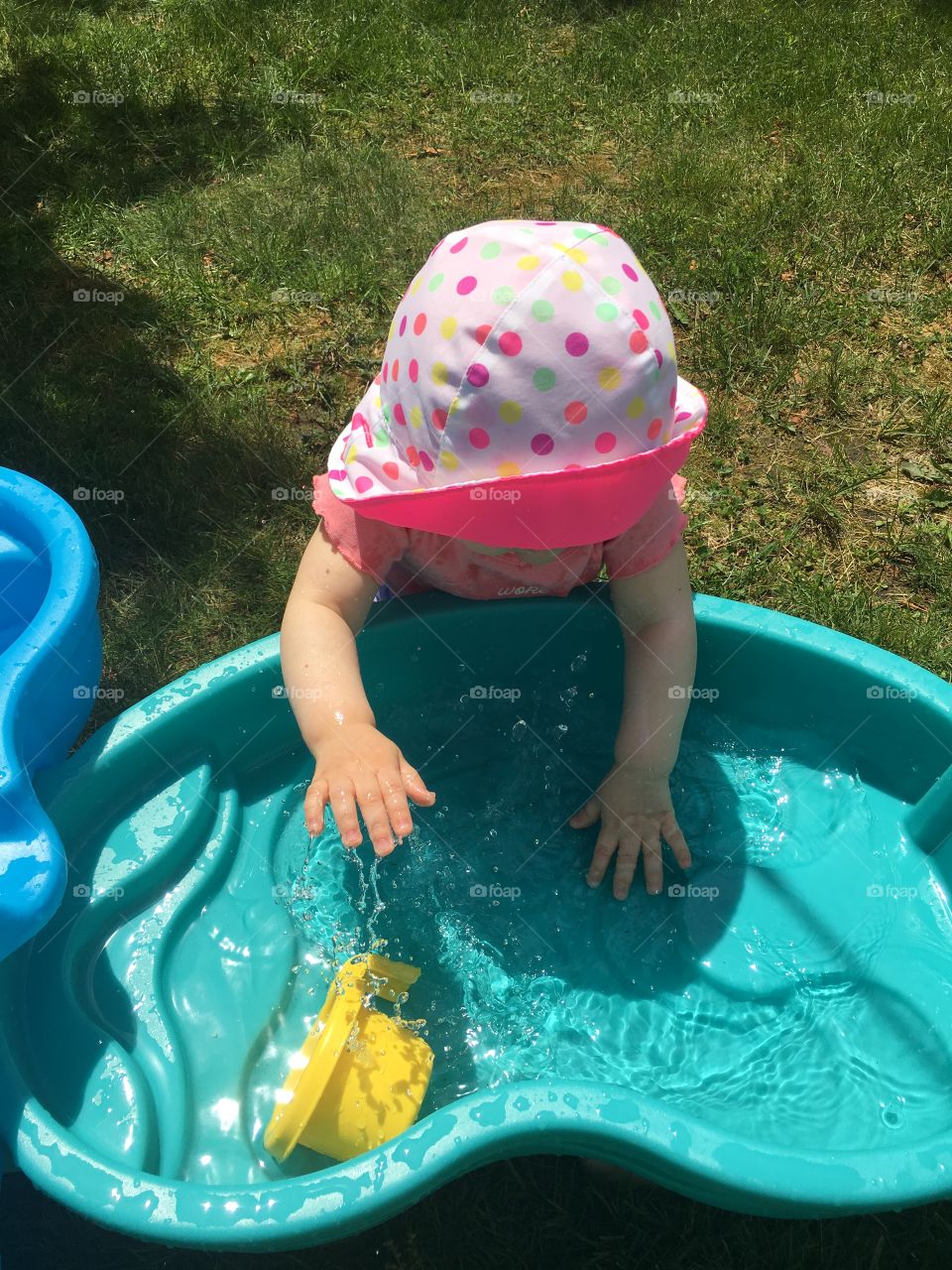 Baby girl splashing in a water table on a sunny summer day