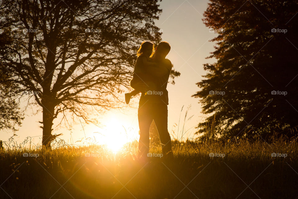 Silhouette of dad and his girl at sunset with trees and meadows