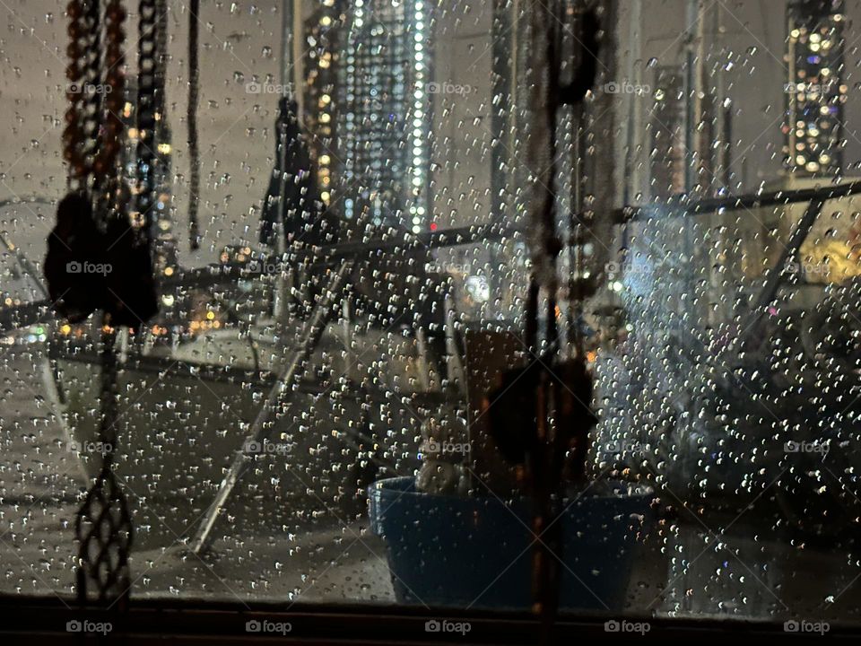 Raindrops are on the window of “Salvation”, the “28 ft 1969 Luhrs” cabin cruiser at “Newtown Creek” in LIC, Queens we both call home and the nighttime illumination of the city gives them a sparkly glittering appearance. 2023. Hypnotic Productions