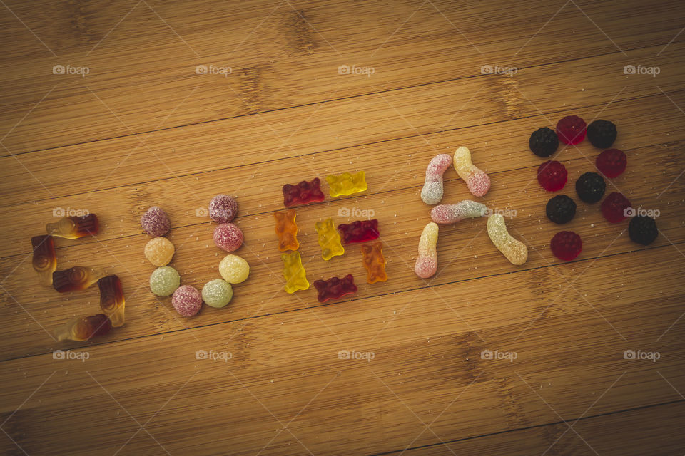 A portrait of the word sugar spelled with different kinds of candy on a wooden table.