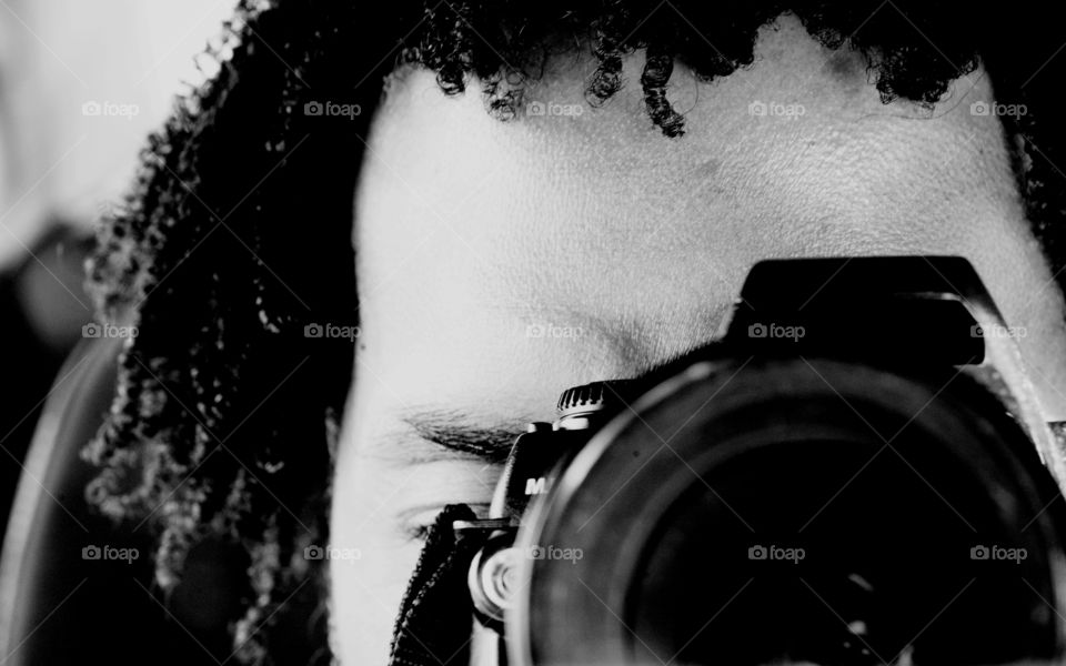 A black and white portrait of a man sitting in a car taking a picture of himself focusing a camera.