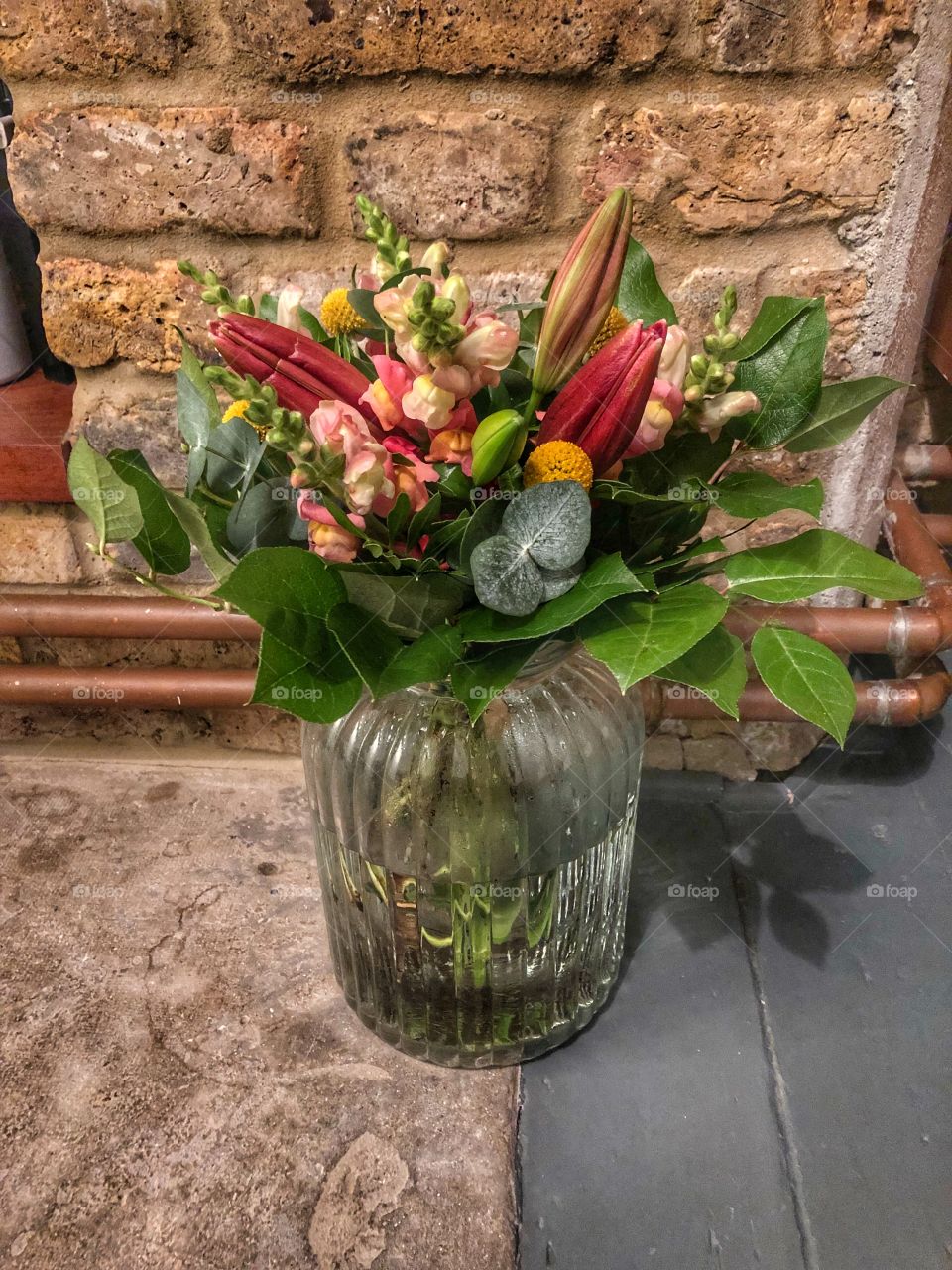 Red, pink, yellow and green floral bouquet on grey painted floorboards with stone coloured exposed brick wall