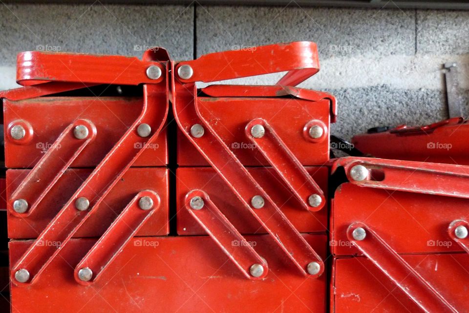 In a garage, red colored toolboxes are closed and stored on a shelf. the wall is made of concrete blocks.