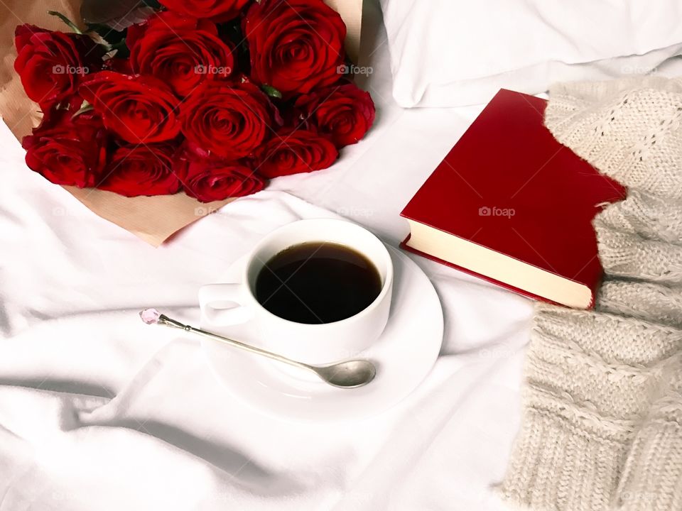 Red roses, red book and coffee cup in white bed 