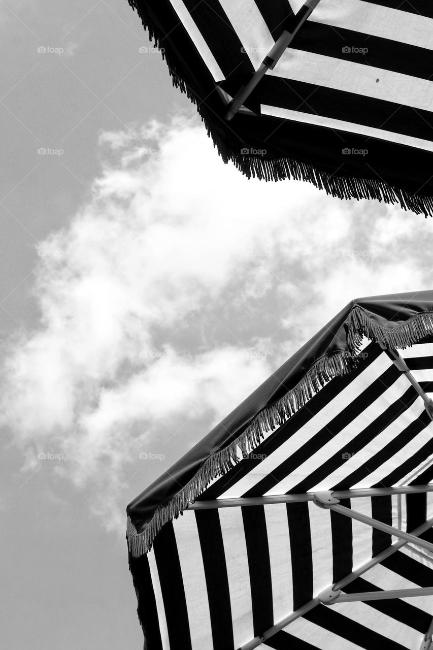 Black and white photo of striped parasols with fringes under sky with cloud