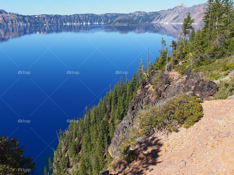 The rugged tree covered slopes of the rim of Crater Lake in Southern Oregon on a sunny and clear summer morning. 