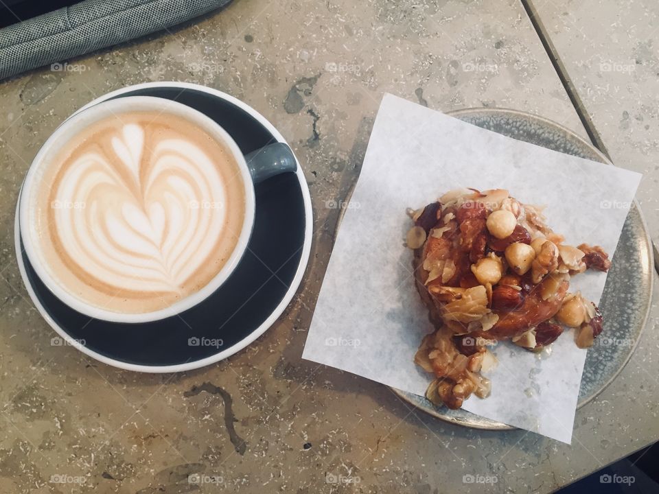Heart decorated cappuccino sits on a table next to a homemade hazelnut snack bar 