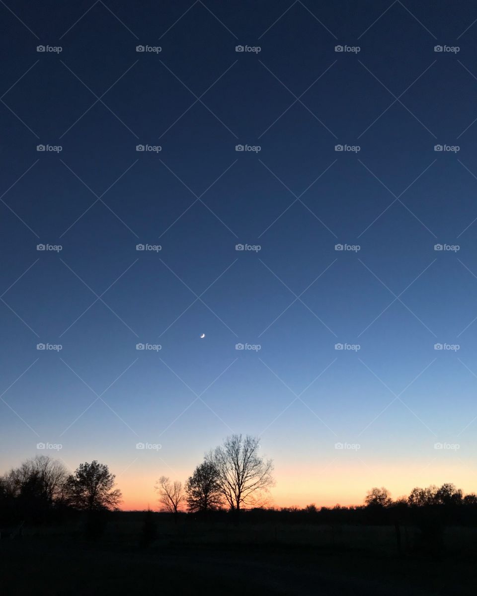 The moon at dusk across a dark blue sky.
