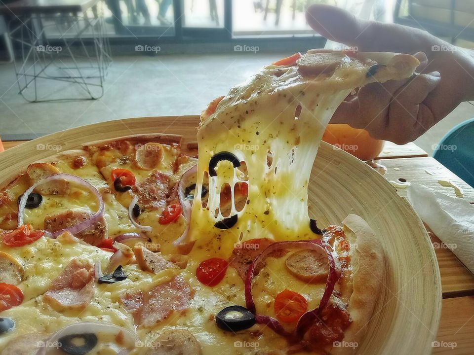 The human hand is picking up a pizza.