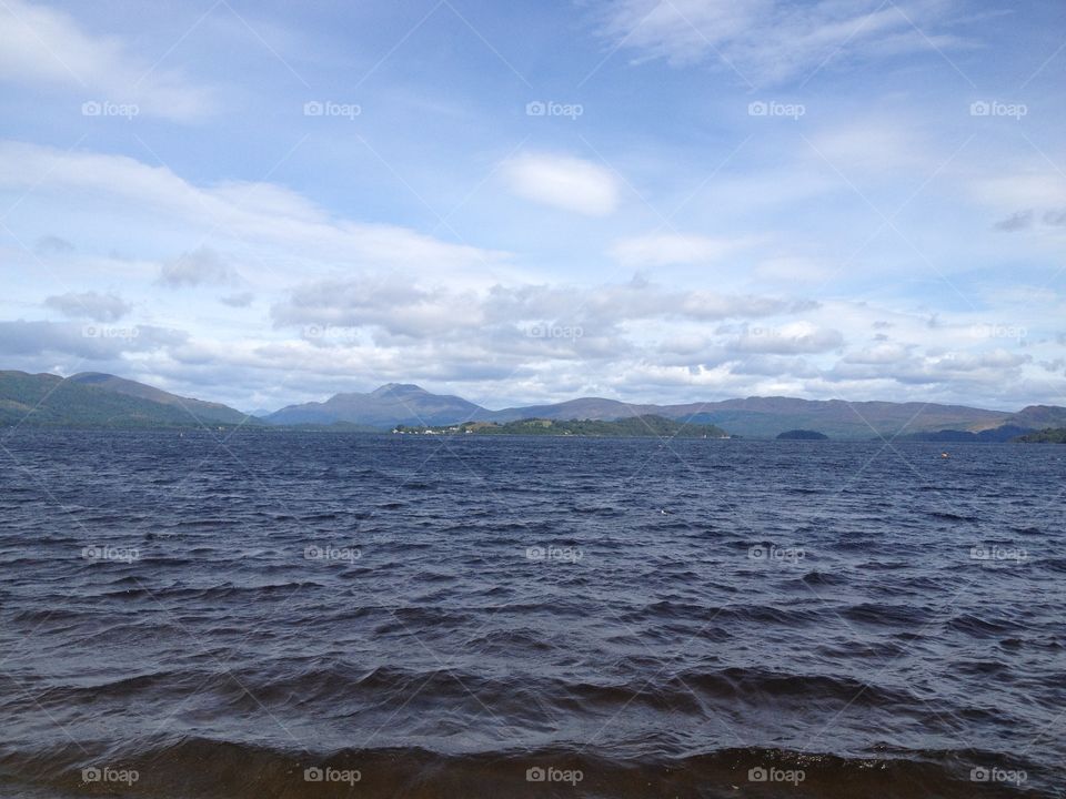 Out at sea with choppy waves and land in the distance. Land ahoy. Choppy water. Swimming in a lake. Bracing water with blue sky above. Scottish loch. Wavy water. Waves at eye level