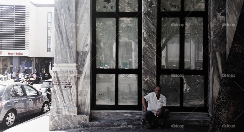 A man resting in the centre of Athens, in a really crowded area with many contradictions and different reflections of reality.