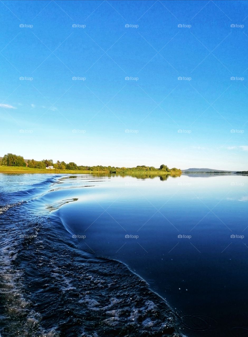 A magnificent image of a calm river with a mirror image of trees and shrubs.