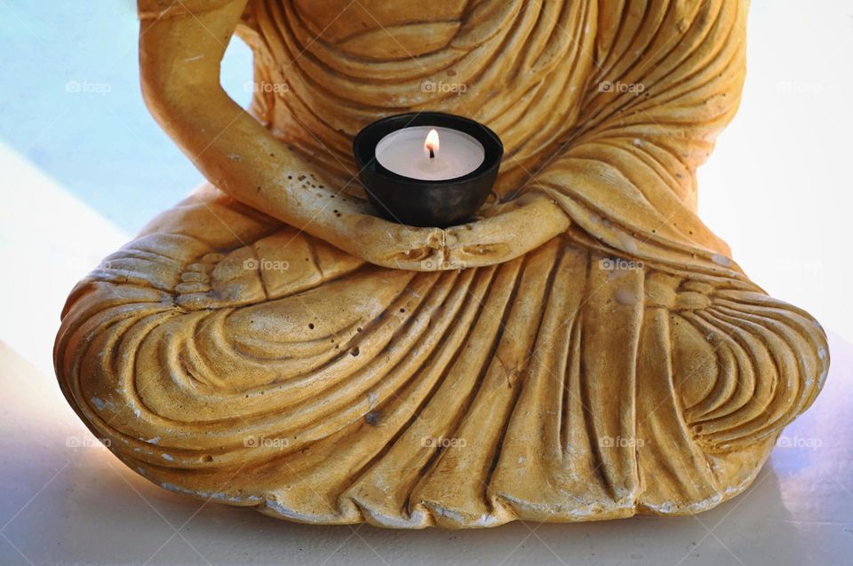 Yellow Buddha body holding a small candle holder with a waxine light burning. Hands buddha, body boeddha, meditation, stillness, mindful
