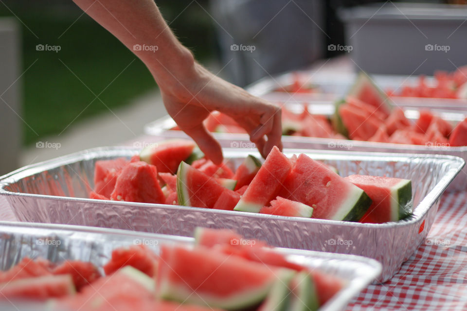 A hand reaches for a fresh piece of watermelon at a summer picnic