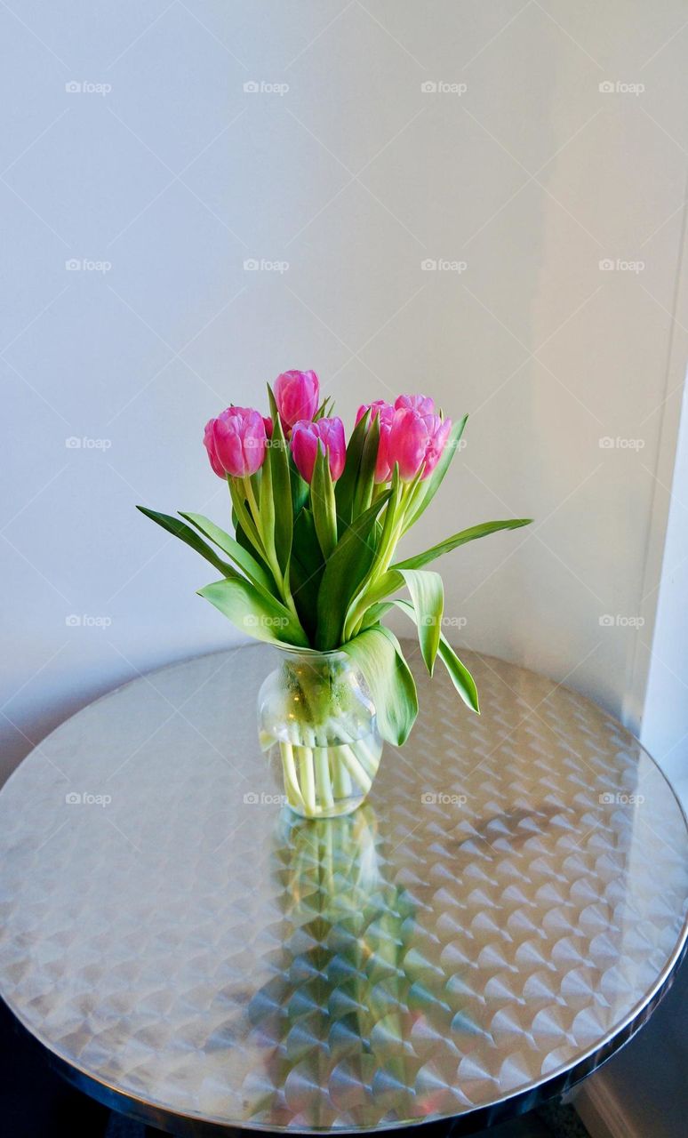 Pink tulips in a vase, on a table, by a window. Tulips are a symbol of rebirth and new beginning. 