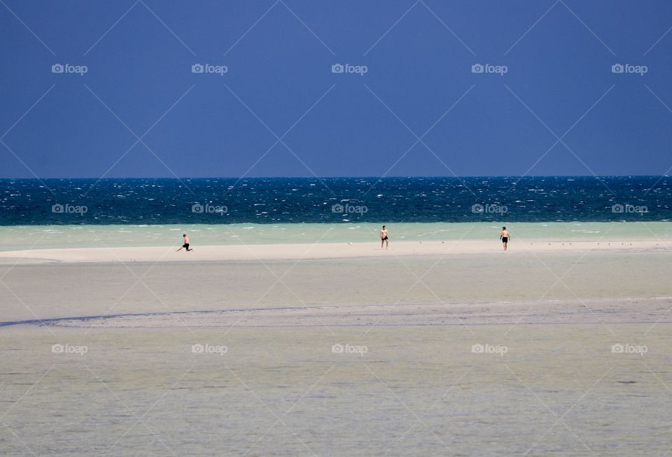 Three people afar off playing on beach at extreme low tide close to ocean horizon