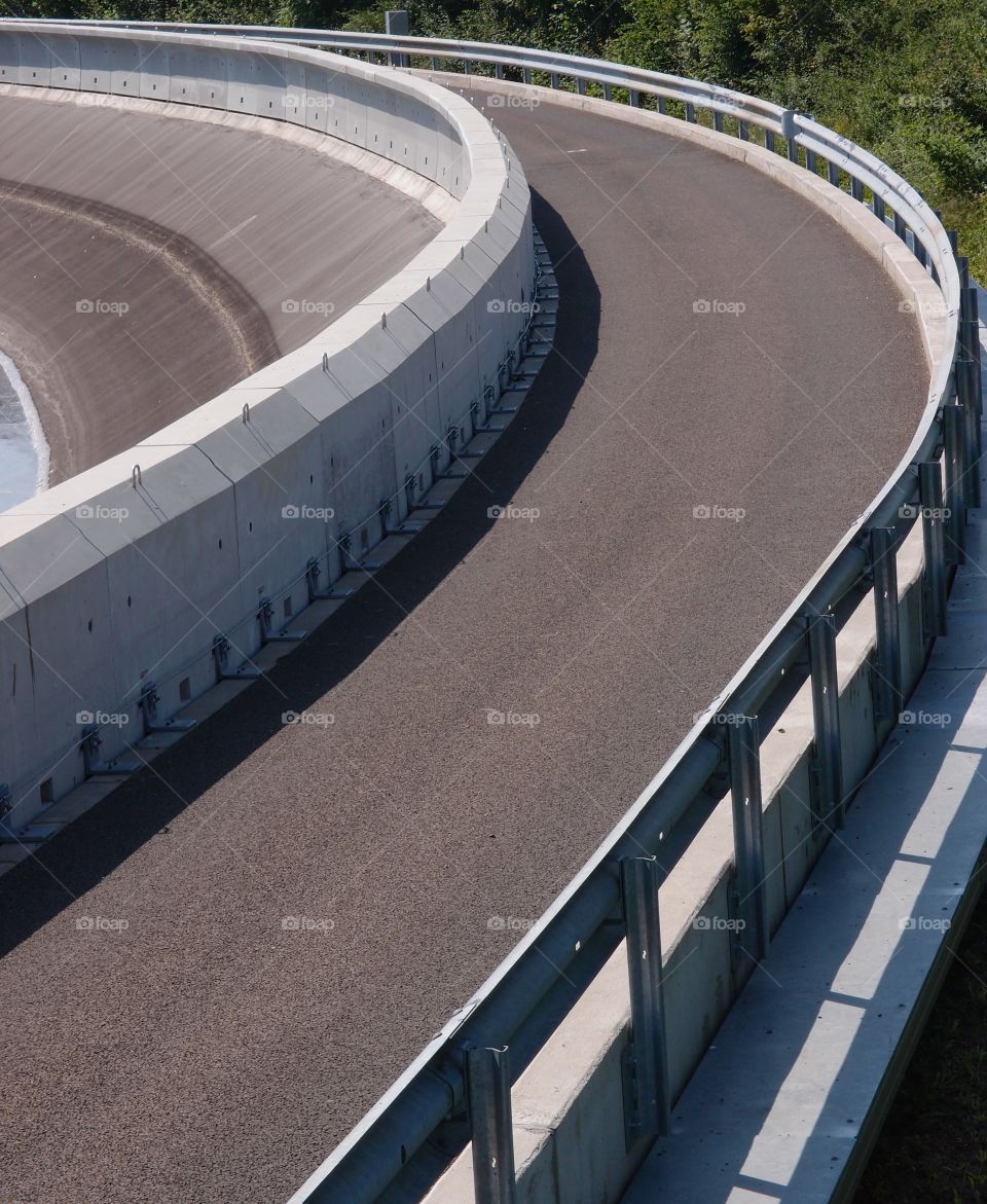 A very skinny road curves around a rounded structure on a sunny summer day. 