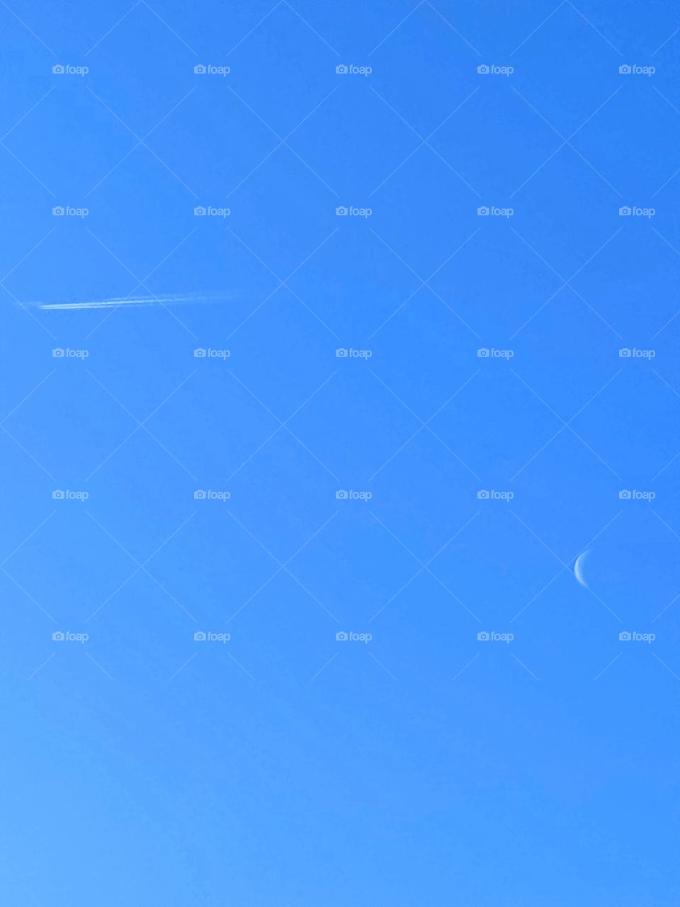 Human and nature. Blue sky. Sunny day. In the sky there is a white crescent moon and a white stripe from a flying plane