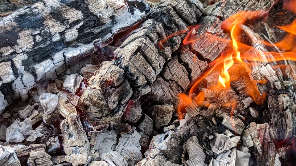 Fire wood, coal and amber ash closeup. Red tongues of flame and glowing amber.