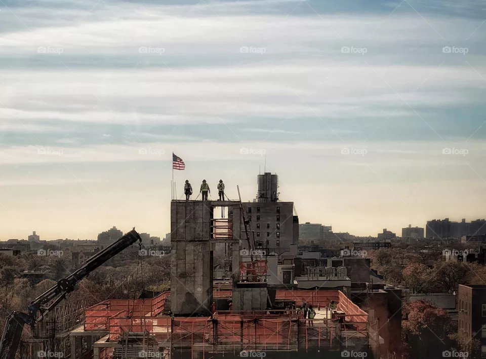 Three workers standing next to the American flag at the top of a building under construction 