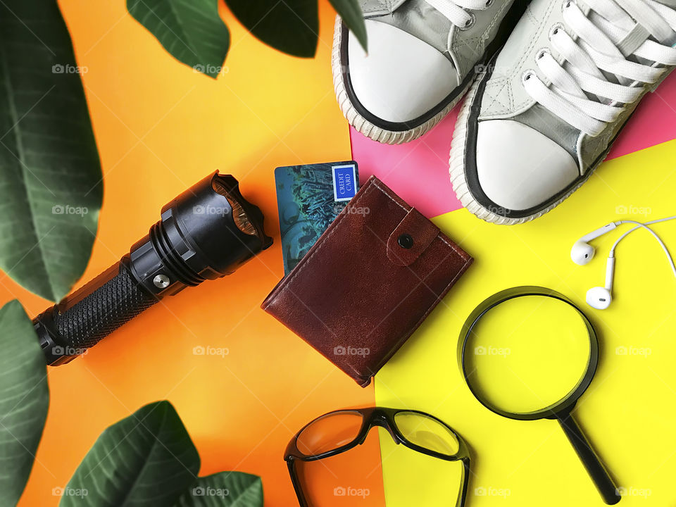 Overheard view of colorful travel items - shoes, wallet, glasses, magnifying glass, flashlight 